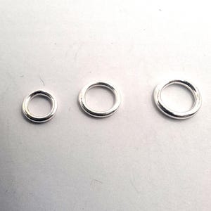 Könnte beinhalten: Drei kreisförmige silberfarbene Metall-Biegeringe, die in einer horizontalen Reihe angeordnet sind und von links nach rechts an Größe zunehmen. Jeder Ring hat eine glatte, polierte Oberfläche mit gleichmäßiger Dicke und einer hohlen Mitte.