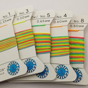 May include: Five spools of colourful embroidery floss, labelled with numbers and sizes in millimetres. The floss is a mix of bright colours, including yellow, orange, green, and blue. The spools are labelled with the Griffin brand name.