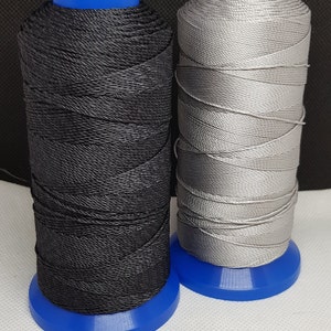 Pu&ograve; includere: Due bobine di filo, una nera e una argentata, sono avvolte su bobine di plastica blu.