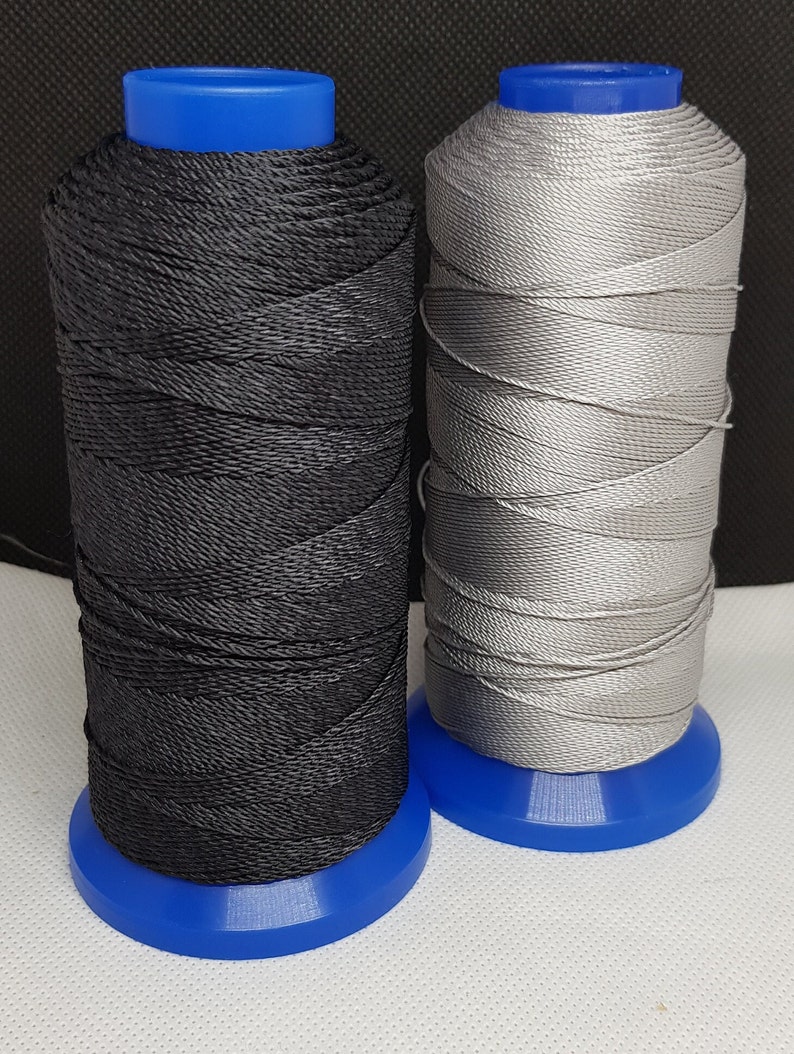 Pu&ograve; includere: Due bobine di filo, una nera e una argentata, sono avvolte su bobine di plastica blu.