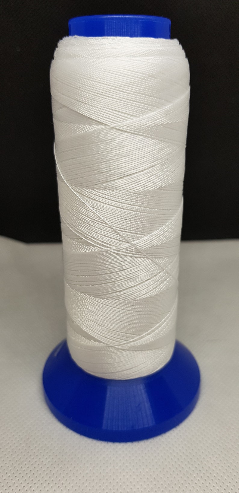 Pu&ograve; includere: Un'bobina di filo bianco avvolta attorno a una bobina di plastica blu.