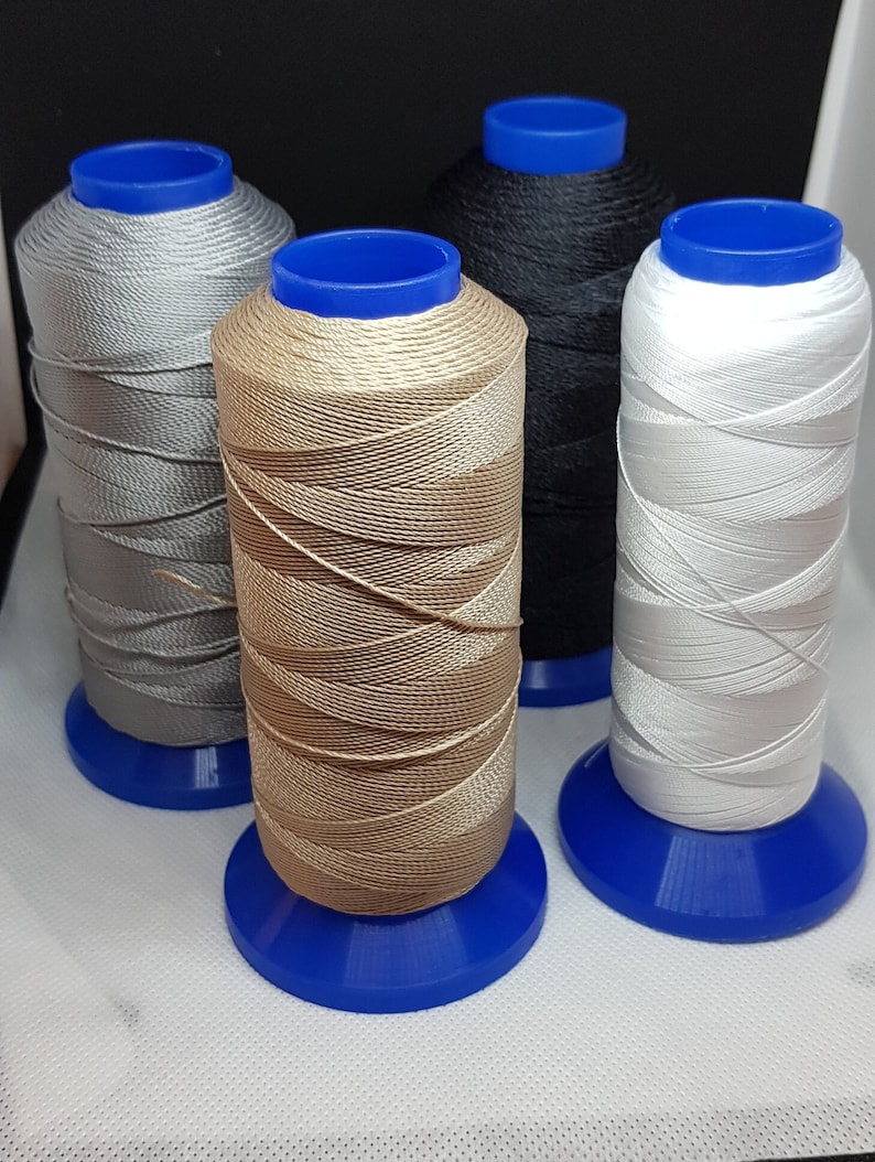 Pu&ograve; includere: Quattro bobine di filo di diversi colori: argento, beige, nero e bianco. Ogni bobina &egrave; su una base di plastica blu.