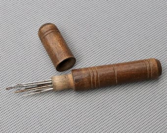 May include: A dark brown wooden needle case with a matching removable cap, featuring a cylindrical shape with horizontal grooves. The case is open, revealing a cluster of thin, silver-colored metal needles protruding from the wooden handle.