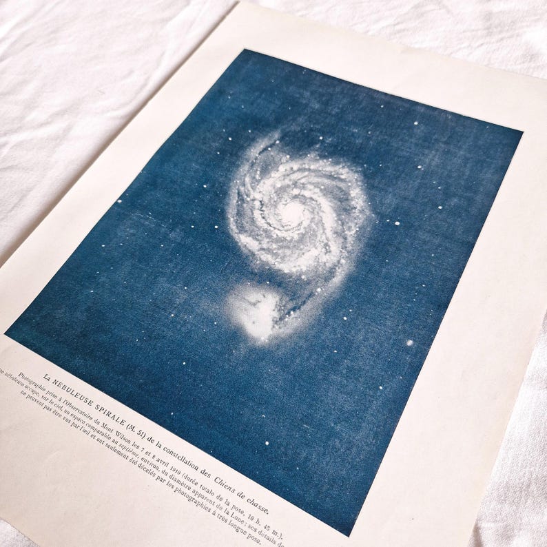 以下が含まれることがあります： 猟犬座にある渦巻銀河M51のヴィンテージな白黒写真。画像は青い背景に白い星が印刷されている。