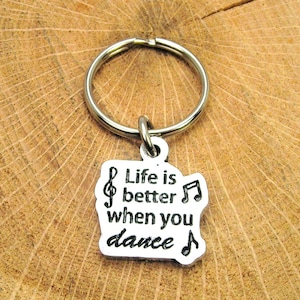 Puede incluir: Llavero de plata con un dije que dice "La vida es mejor cuando bailas" con notas musicales.