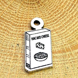 May include: Silver charm shaped like a box of mac and cheese. The box has a white background with black text that reads "Mac and Cheese". There is a black and white illustration of a slice of cheese and a bowl of mac and cheese on the front of the box.