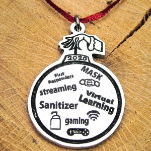 May include: Silver Christmas ornament with the year 2020 and the words "MASK", "First Responders", "streaming", "Sanitizer", "gaming", "Virtual Learning" and icons representing each word.