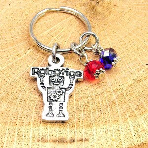 May include: A silver keychain with a robot charm and the word "Robotics" above it. The keychain has two crystal beads, one red and one blue.