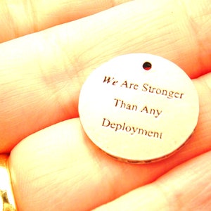 May include: A round, silver-colored metal tag with the words "We Are Stronger Than Any Deployment" engraved on it.