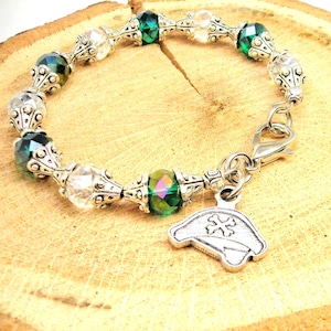 Può includere: Un braccialetto con perline di cristallo verde e trasparente con un ciondolo d'argento a forma di cappello con una croce in cima.