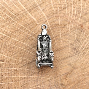 Puede incluir: Encanto de plata de un trono con una calavera en la parte posterior. El trono tiene un diseño detallado con reposabrazos y un reposapiés.