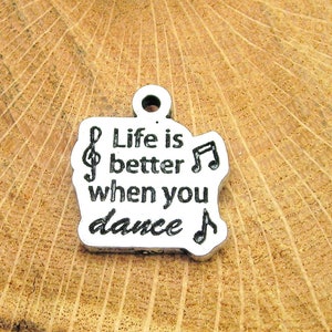 Puede incluir: Encanto de plata con el texto "Life is better when you dance" y notas musicales.