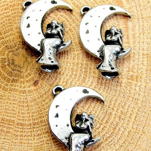 May include: Three silver charm pendants featuring a crescent moon with a small angel sitting on top. The angel is depicted with wings and a flowing gown.