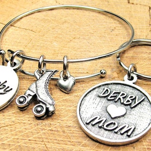 Può includere: Braccialetto in argento con un ciondolo a forma di pattini a rotelle, un ciondolo a forma di cuore e un ciondolo rotondo che dice "Derby girl". Un portachiavi in argento con un ciondolo rotondo che dice "Derby Mom" con un cuore.