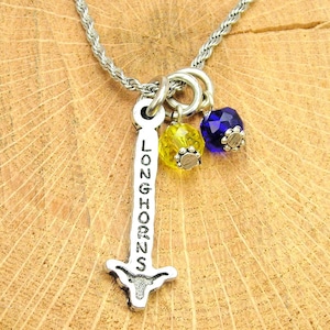 May include: A silver necklace with a charm that says "Longhorns" and a small silver bull's head. The charm is attached to two small beads, one blue and one yellow.