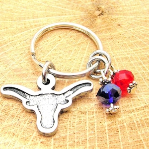 May include: A silver key ring with a bull's head charm and two dangling beads, one red and one blue.