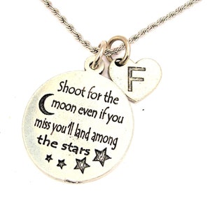 Puede incluir: Collar de plata con un colgante redondo que dice "Shoot for the moon even if you miss you'll land among the stars" y un pequeño colgante de corazón con la letra "F" en él.