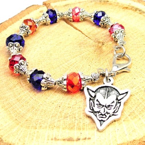 May include: A silver charm bracelet with red, blue, and orange crystal beads and a silver devil head charm.