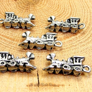 May include: Five silver-toned train charms with a detailed design. Each charm features a locomotive with wheels and a chimney.