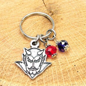 May include: A silver keychain with a devil face charm, a red crystal bead, and a blue crystal bead.