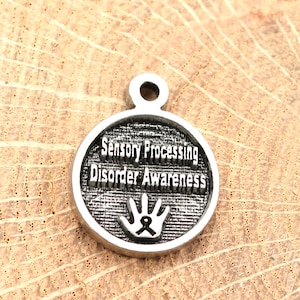 以下が含まれることがあります： 「Sensory Processing Disorder Awareness」というテキストとリボンが付いた手のひら型のシルバーチャーム