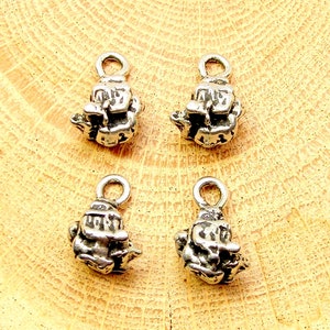May include: Four silver charm pendants in the shape of a small house with a detailed textured surface. Each charm has a loop at the top for attaching to a necklace or bracelet.