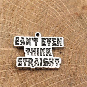 May include: Silver-colored metal charm with the text "CAN'T EVEN THINK STRAIGHT" in bold, uppercase letters. The charm has a small loop at the top for attaching to a necklace or bracelet. The charm is set against a wooden background.