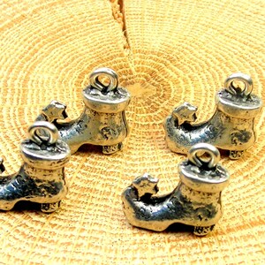 Könnte beinhalten: Vier silberne Elfen-Schuh-Anhänger mit einem Stern an der Spitze. Die Anhänger haben eine Schlaufe oben zum Anbringen an einer Halskette, einem Armband oder anderem Schmuck.