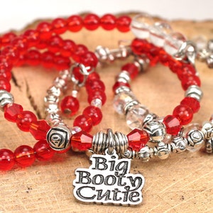 May include: Set of four bracelets with red and clear glass beads and silver accents. One bracelet has a charm that says "Big Booty Citie". Another bracelet has a heart charm.