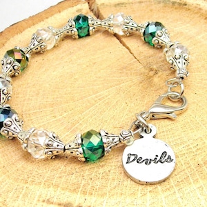 Puede incluir: Un brazalete de plata con cuentas de cristal verde y transparente y un dije de plata que dice "Devils".