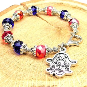 May include: A silver charm bracelet with red, blue and clear crystal beads. The charm is a silver pirate head with a skull and crossbones.