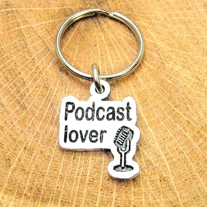 Może przedstawiać: Srebrny brelok do kluczy z zawieszką w kształcie mikrofonu i napisem "Podcast lover".