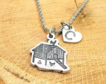 Può includere: Una collana d'argento con due ciondoli: un piccolo cuore con la lettera "C" e un ciondolo dettagliato di un pollaio con un gallo in cima.