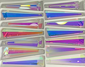 Peut inclure: Un plateau de prismes en cristal irisé. Chaque prisme est de forme triangulaire allongée avec de multiples facettes, reflétant un spectre de couleurs comprenant le bleu, le violet, le rose et le jaune. Les prismes sont disposés en grille dans des compartiments individuels.