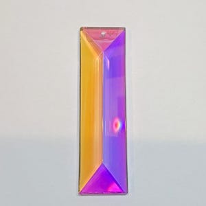 May include: A rectangular prism-shaped crystal pendant with a hole at the top for hanging. The crystal is divided into two sections, one side is a golden-yellow color, and the other is a vibrant purple. The crystal has a faceted design.