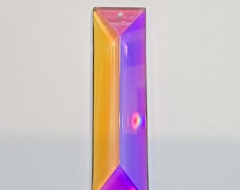 Peut inclure: Un pendentif en cristal en forme de prisme rectangulaire avec un trou en haut pour l'accrocher. Le cristal est divisé en deux sections, un côté est de couleur jaune doré et l'autre est violet vif. Le cristal a un design à facettes.