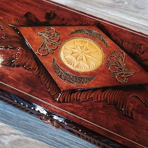 May include: A wooden box with a decorative inlay of gold filigree and a carved star design. The box has a dark brown stain and a glossy finish.