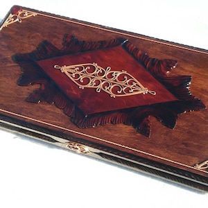 May include: A wooden game box with a red and gold inlay design. The box has a hinged lid and is decorated with intricate carvings.