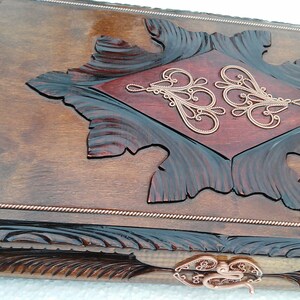 May include: A wooden game board with intricate carvings and copper accents. The board has a dark brown stain and a red inlay in the center. The copper accents are in the shape of swirls and are around the edges of the board.
