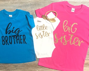 Puede incluir: Tres camisetas con las palabras "hermano mayor", "hermana pequeña" y "hermana mayor" impresas en ellas. Las camisetas son azul, blanca y rosa.