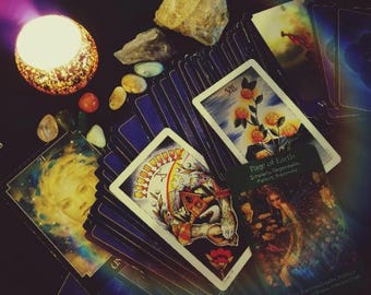 May include: A collection of tarot cards with various illustrations, including a card with the text "Page of Earth". The cards are arranged with crystals, stones, and a lit candle in a decorative holder. The color palette is dark with warm highlights.