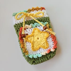 May include: A handmade crochet phone case in shades of green, white, yellow, orange, and brown. The case features a yellow star applique and a yellow drawstring closure with wooden beads. The case is approximately 6 inches tall.