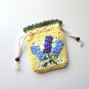 May include: A small crocheted drawstring bag with a floral design. The bag is yellow with green, blue, and purple flowers. The bag has a white drawstring.