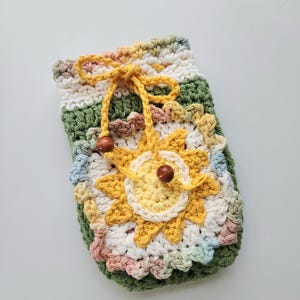 May include: A handmade crochet pouch in shades of green, yellow, white, and pink. The pouch features a large sunflower applique and a drawstring closure with wooden beads. The overall design is a mix of textures and colors.