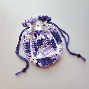 May include: A small purple and white crocheted drawstring bag with a white cord and wooden beads.