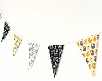May include: A decorative bunting banner with triangular flags. The flags feature various patterns, including owls, lions, and floral designs, in colors like black, white, yellow, and gray. The flags are strung together on a white cord, creating a festive look.