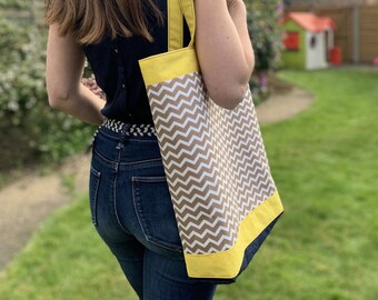 May include: A woman is carrying a brown and white chevron patterned tote bag with yellow straps. The bag has a yellow trim around the top.