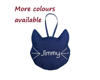 May include: A navy blue cat-shaped plush ornament with the name "Jimmy" embroidered in white thread.