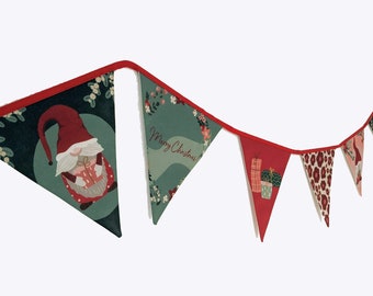 May include: A festive Christmas banner with triangular flags. The flags feature various designs, including a gnome holding a gift, the words "Merry Christmas," gift boxes, and a leopard print pattern. The banner is trimmed with red fabric.