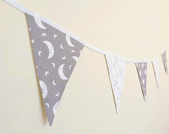 May include: A gray and white fabric bunting with a moon and star pattern. The bunting is strung on a white ribbon and is hanging on a wall.